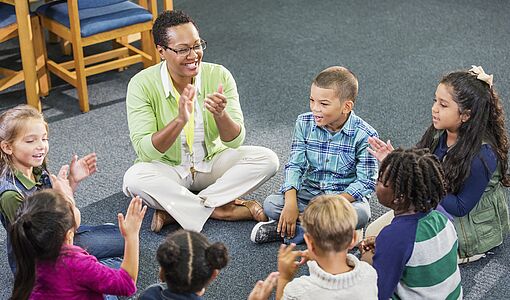 Lehrerin mit Schülern im Sitzkreis klatschend