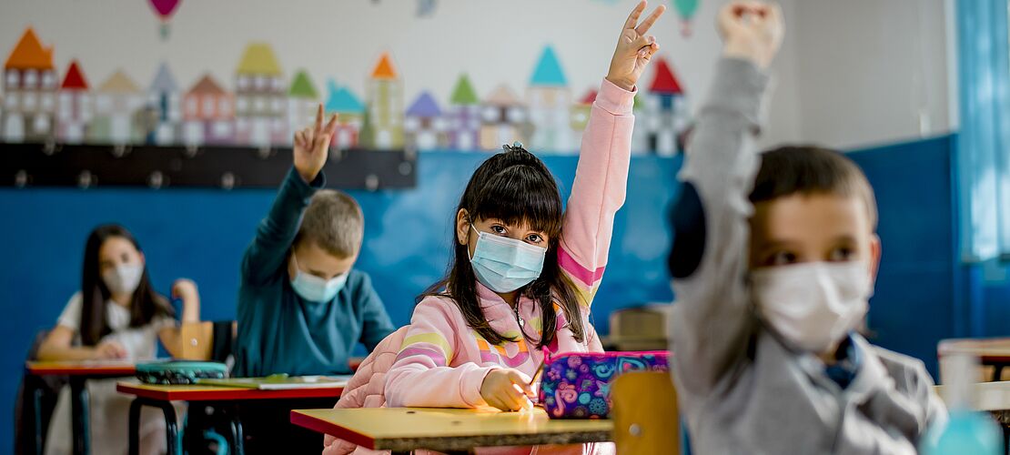 Kinder in einer Klasse zeigen auf