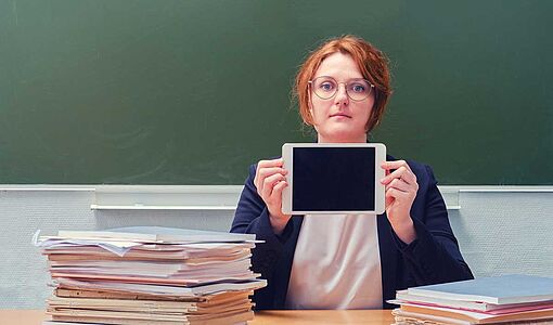 Lehrerin sitzt an einem Tisch mit einem Tablet in den Händen