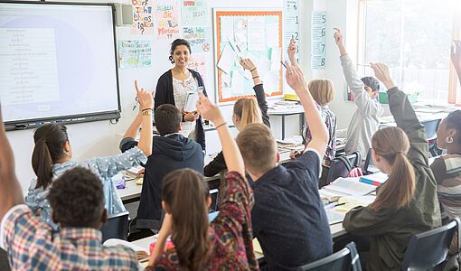 Klasse im Klassenzimmer, die Schüler zeigen auf