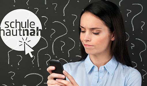 Lehrerin vor der Tafel mit dem Handy in der Hand, macht ärgerliches Gesicht