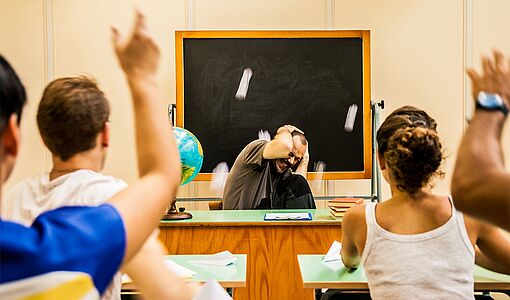 Schüler bewerfen den sich schützenden Lehrer mit Kreide