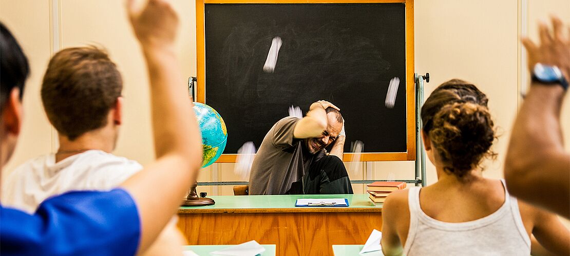 Schüler bewerfen den sich schützenden Lehrer mit Kreide