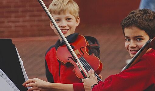 Zwei Jungs im roten Langarmhemd spielen Geige und Cello
