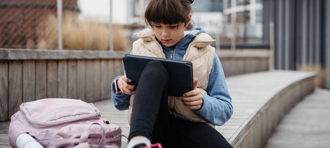 Kind sitzt vor Schule und surft im Internet