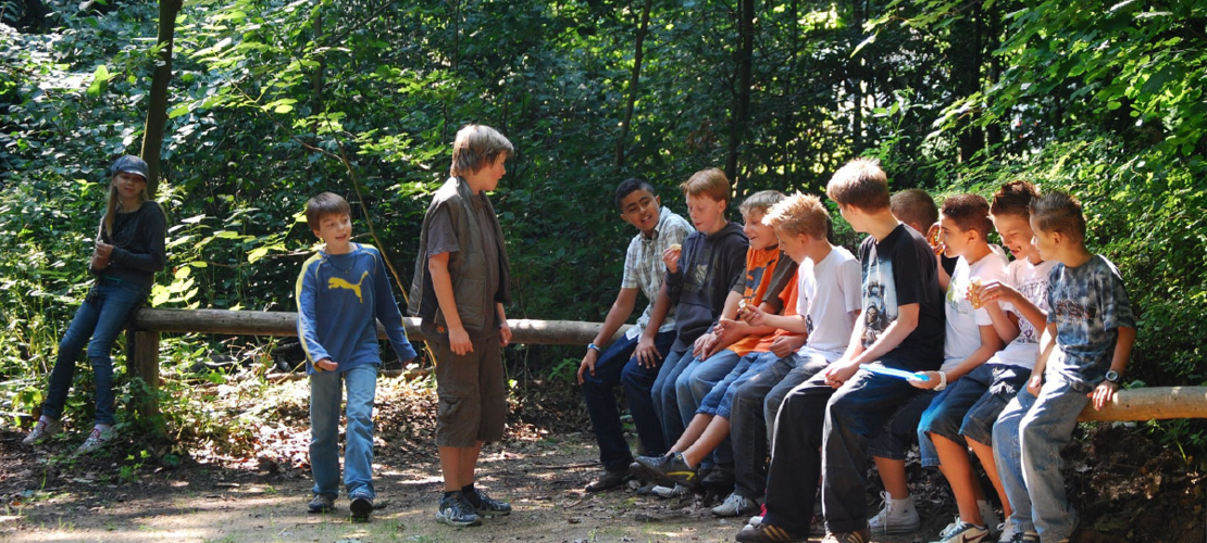 Eine Gruppe von Kindern sitzt auf einem Baumstamm und unterhält sich.