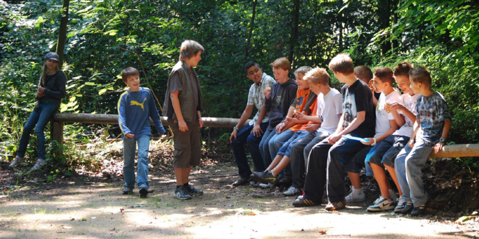 Eine Gruppe von Kindern sitzt auf einem Baumstamm und unterhält sich.
