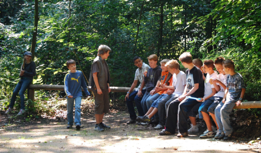 Eine Gruppe von Kindern sitzt auf einem Baumstamm und unterhält sich.