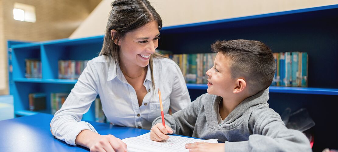 Lehrerin sitzt mit Schüler am Tisch und erklärt etwas