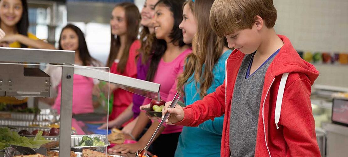 Schüler stellen sich beim Mittagessen in der Schulküche an