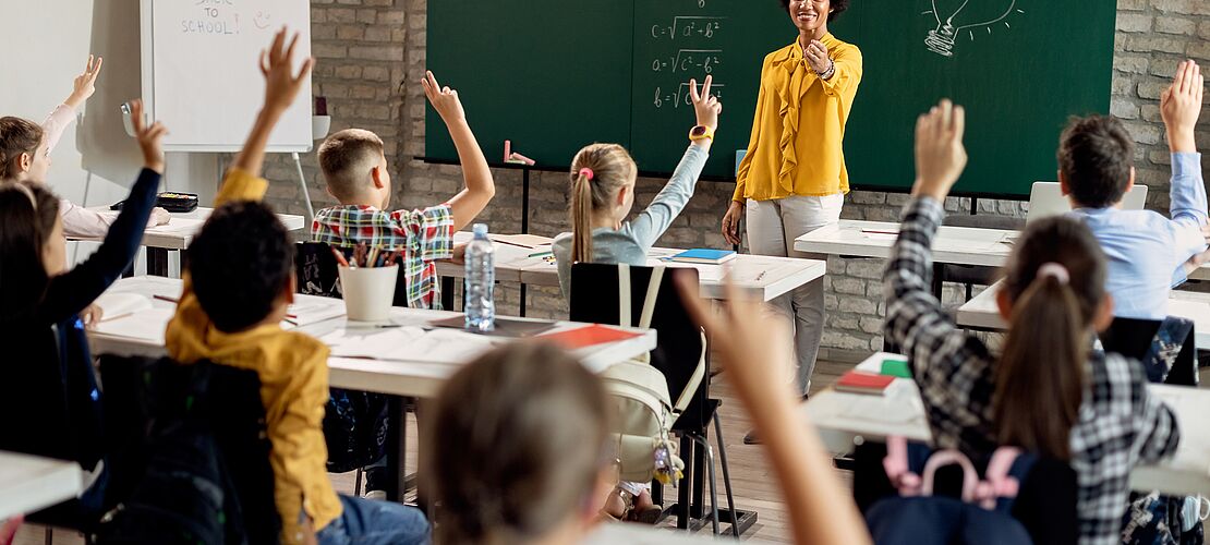 Kinder während des Unterrichts mit Lehrerin, einige zeigen auf