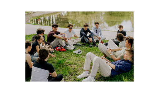 ©Verein Philolympics Austria - Philosophieolympiade Jugendliche sitzen im Kreis auf einer Wiese am Wasser und unterhalten sich.