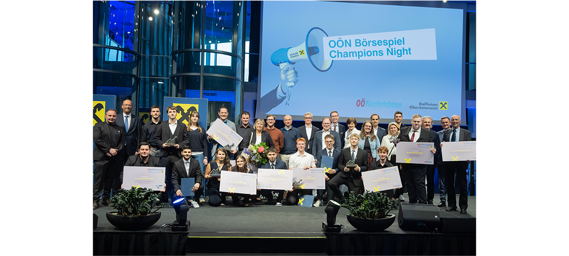 Viele Personen stehen und sitzen gemeinsam auf einer Bühne und halten Urkunden vor einer großen Leinwand mit dem Text „OÖN Börsespiel Champions Night“.