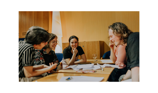 Fünf Jugendliche sitzen gemeinsam an einem Tisch, lachen und arbeiten an Unterlagen.
