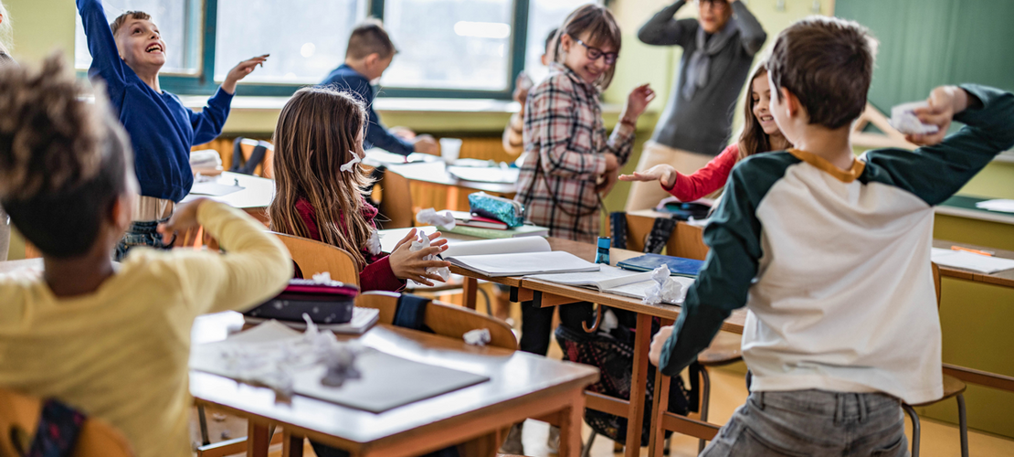 Eine große Gruppe von Schulkindern macht während eines Unterrichts im Klassenzimmer Chaos, während ihr Lehrer darüber frustriert ist.