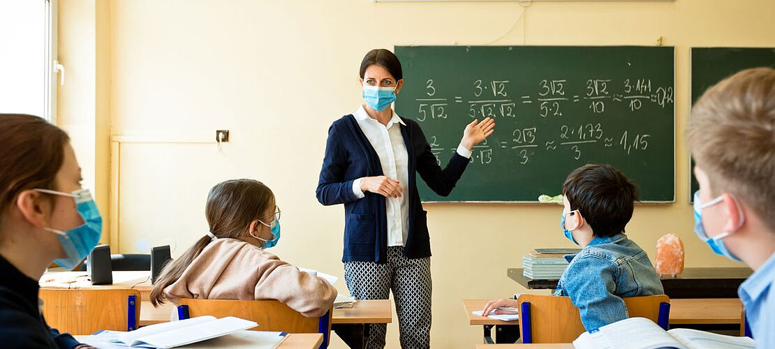 Lehrerin mit Maske in der Klasse vor einer Tafel