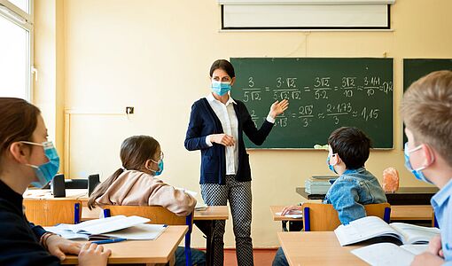 Lehrerin mit Maske in der Klasse vor einer Tafel