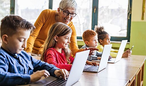 Lehrerin erklärt Schülern etwas am Laptop