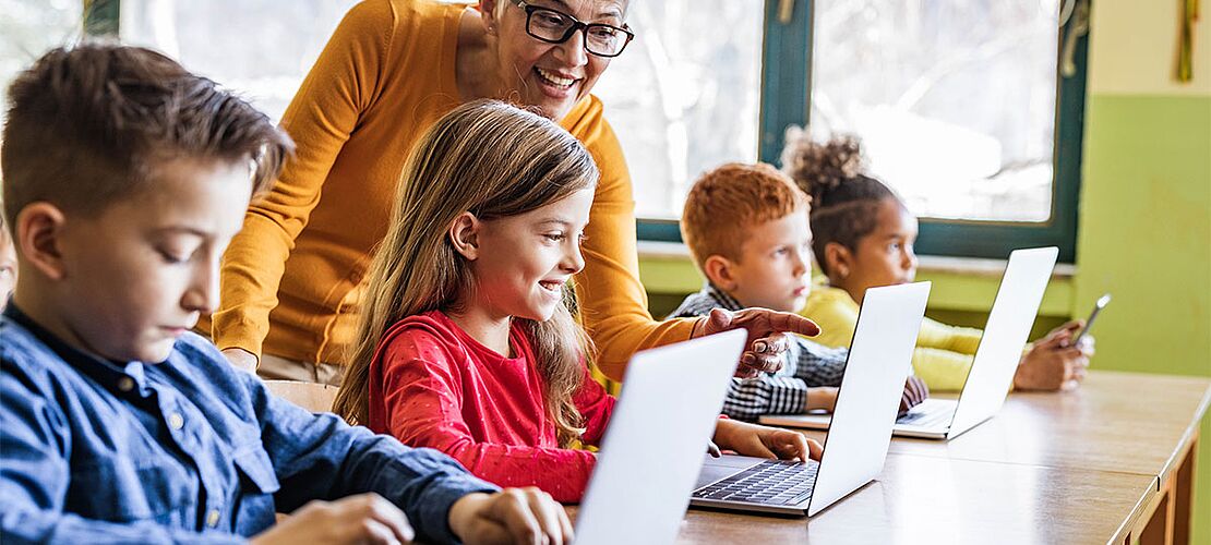 Lehrerin erklärt Schülern etwas am Laptop