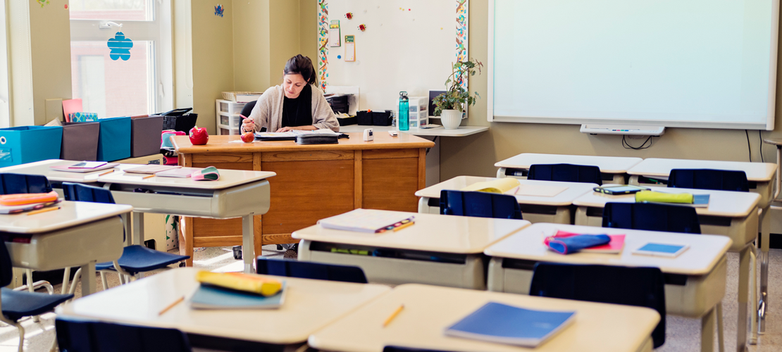 Lehrerin arbeitet an ihrem Schreibtisch im leeren Klassenzimmer