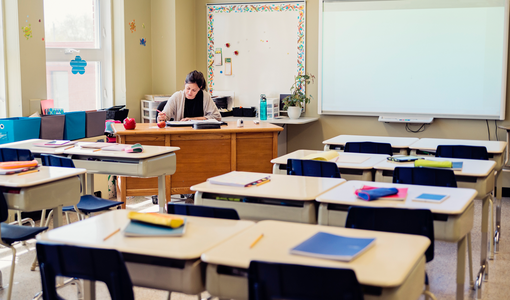 Lehrerin arbeitet an ihrem Schreibtisch im leeren Klassenzimmer