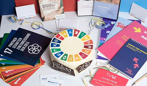 Geburtstagstorte, Flyer und Bücher bzw. Bildungsmaterialien rund um die 17 Nachhaltigskeitsziele der Agenda 2030 der Vereinten Nationen