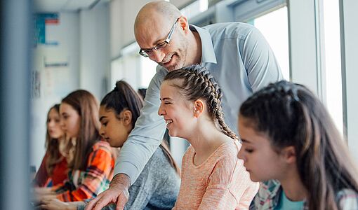 Lehrer erklärt Schülerinnen gerade etwas am Computer