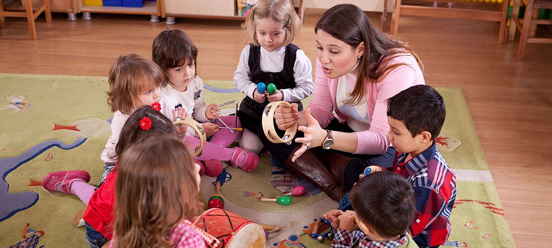 Gruppe von Kindern mit Elementarpädagogin im Kindergarten