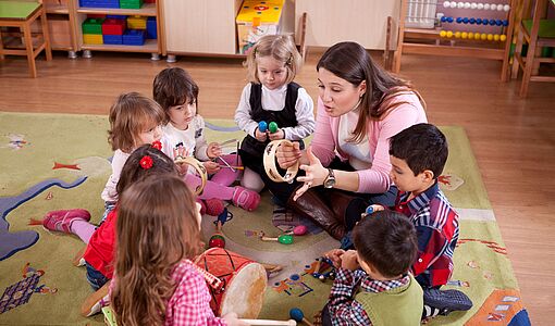 Gruppe von Kindern mit Elementarpädagogin im Kindergarten