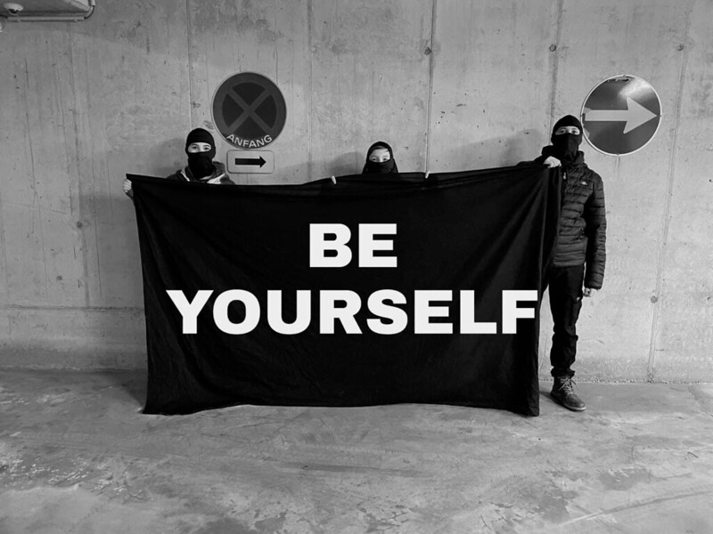 3 Schüler halten ein schwarzes Plakat mit der Aufschrift: Be Yourself